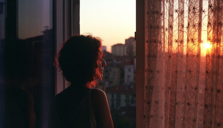 Woman looking out window at sunset over city